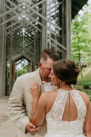 A tender moment between newlyweds under an architectural glass ceiling in a forest setting.