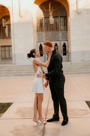 A couple shares playful dance poses in front of a grand archway during a wedding photoshoot.