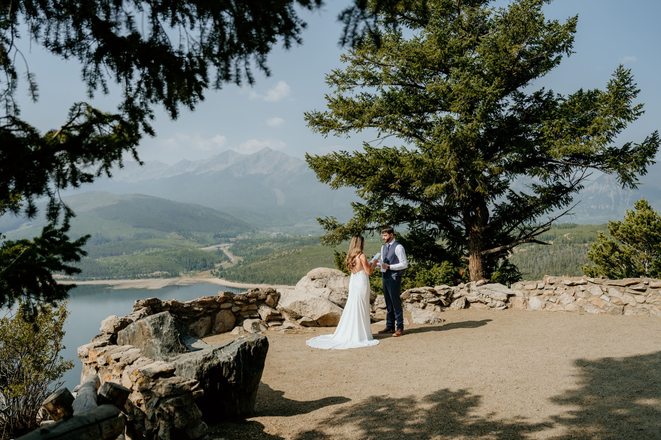 Wedding couple poses on scenic mountain overlook with evergreen trees.