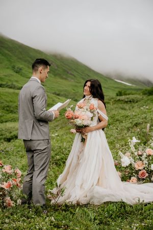 Wedding ceremony in a lush green mountainside with fog and a beautiful floral bouquet.