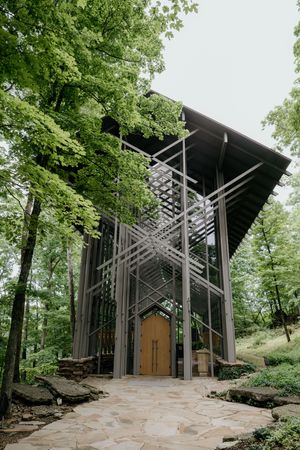 A modern glass and steel chapel structure nestled among green forest trees.