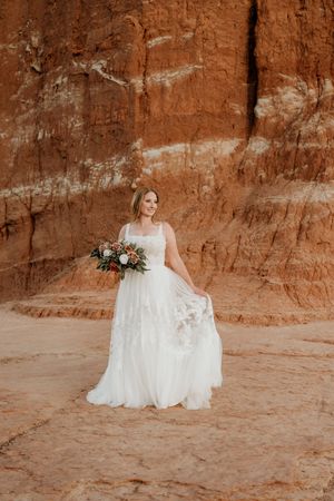 A bride in a lace gown photographed against rustic red canyon walls.