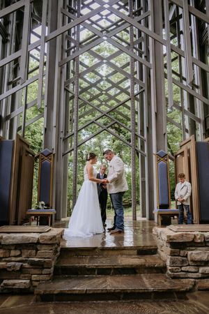 Wedding ceremony inside a geometric glass chapel with stone foundation.