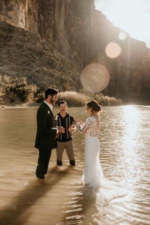 A wedding ceremony taking place along a river bank with towering canyon walls.