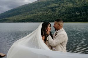 A romantic lakeside wedding moment with mountains and cloudy skies in the background.