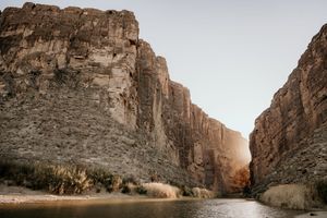 Dramatic canyon walls tower over a winding river at sunset.
