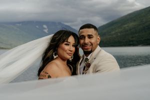 A romantic wedding portrait with a flowing veil against a mountain lake backdrop.
