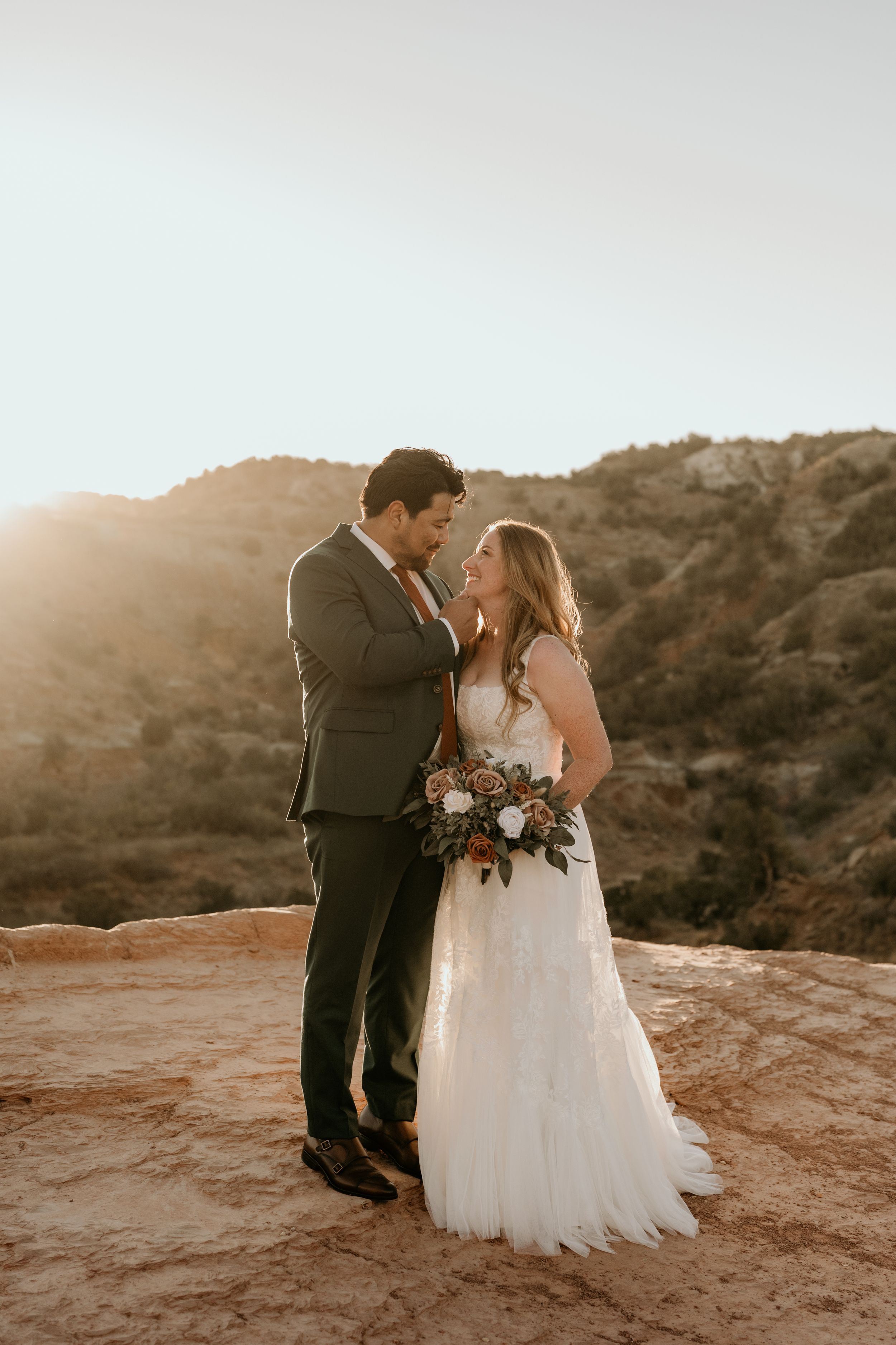 Couple shares intimate moment on red rocks during sunset wedding photoshoot.