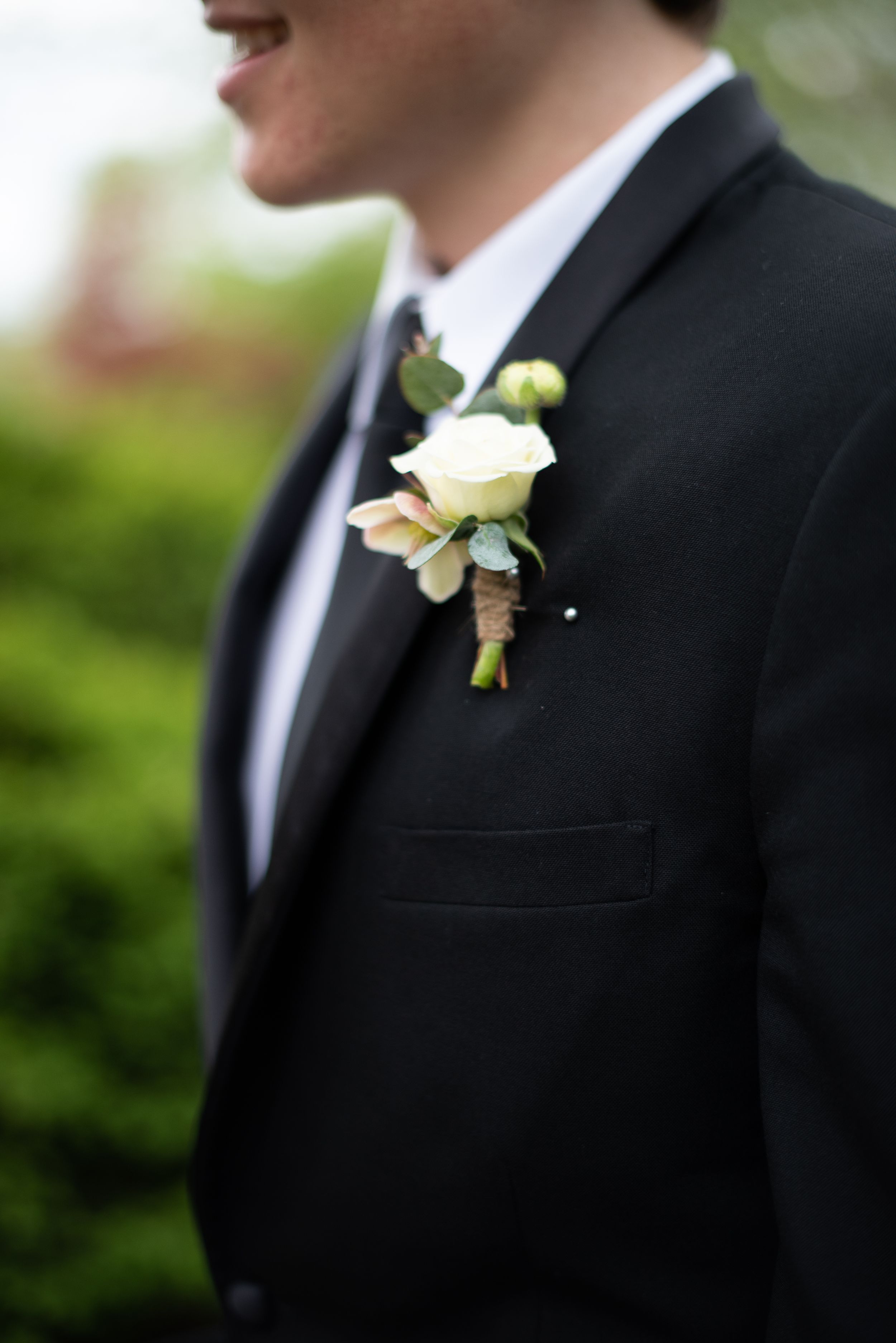 A white rose boutonniere adorns the lapel of a black tuxedo jacket at a formal event.