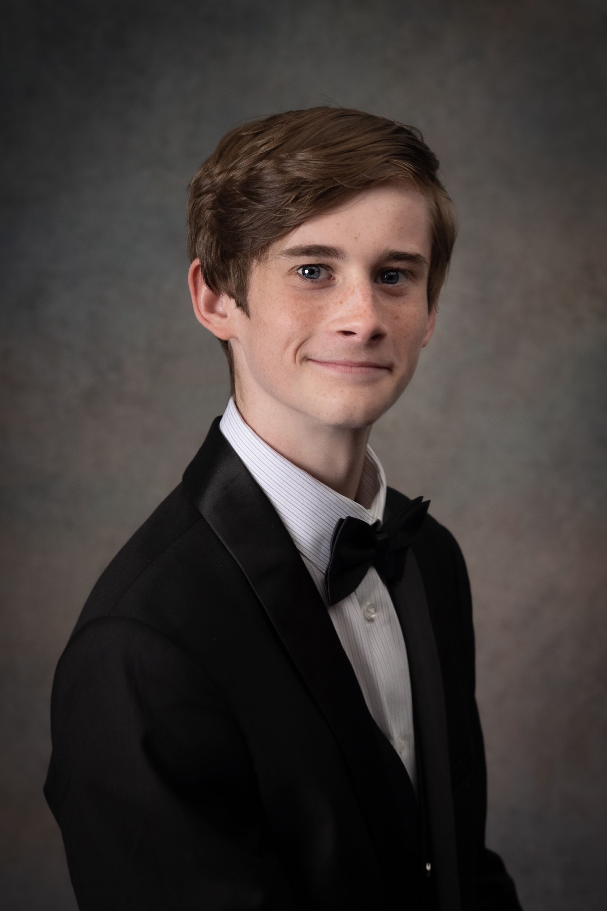Professional headshot portrait series of someone in a black suit and tie against a dark gray studio backdrop.