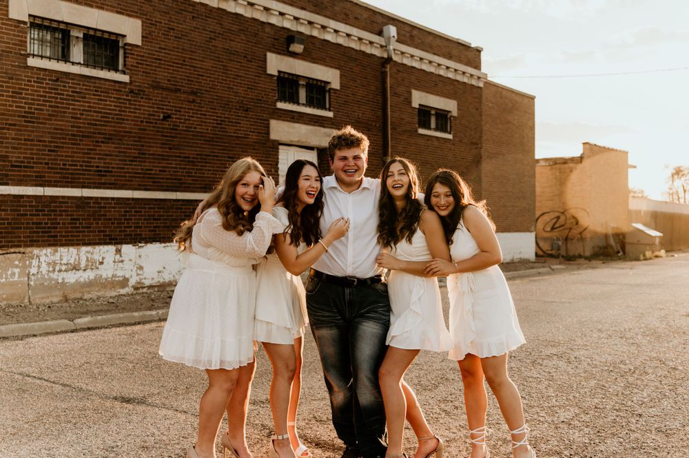 A group poses in front of a brick building wearing coordinated white outfits and jeans.