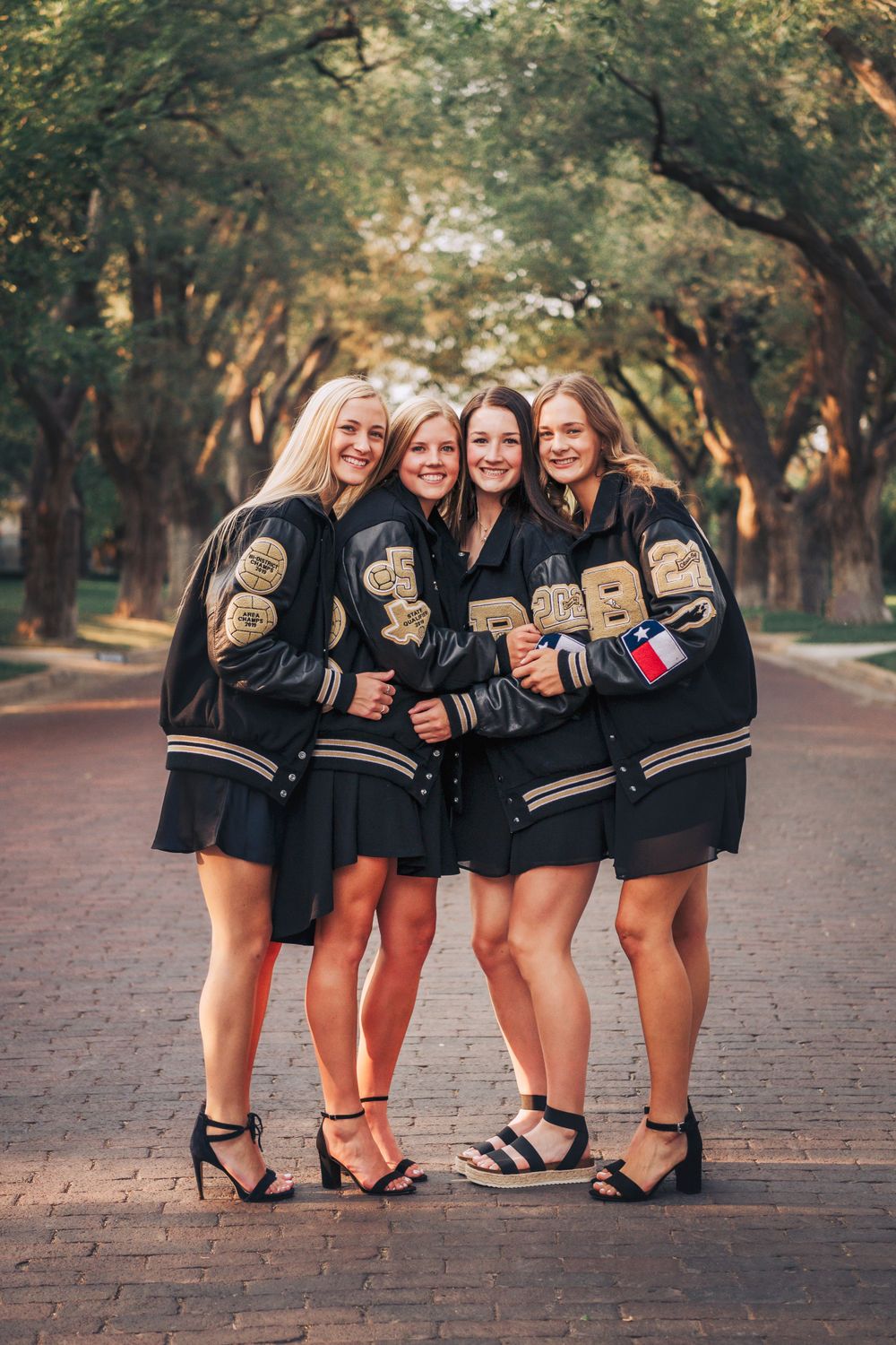 A group shows off their decorated graduation caps while posing on a brick pathway.