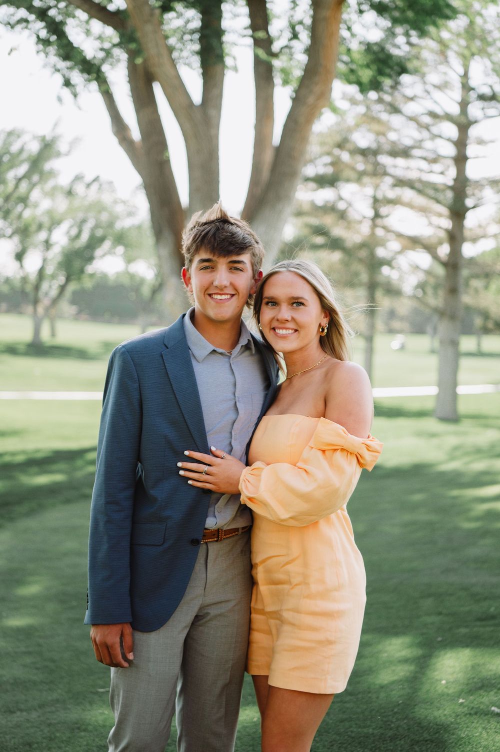 Couple poses together on grassy lawn during spring engagement photoshoot.