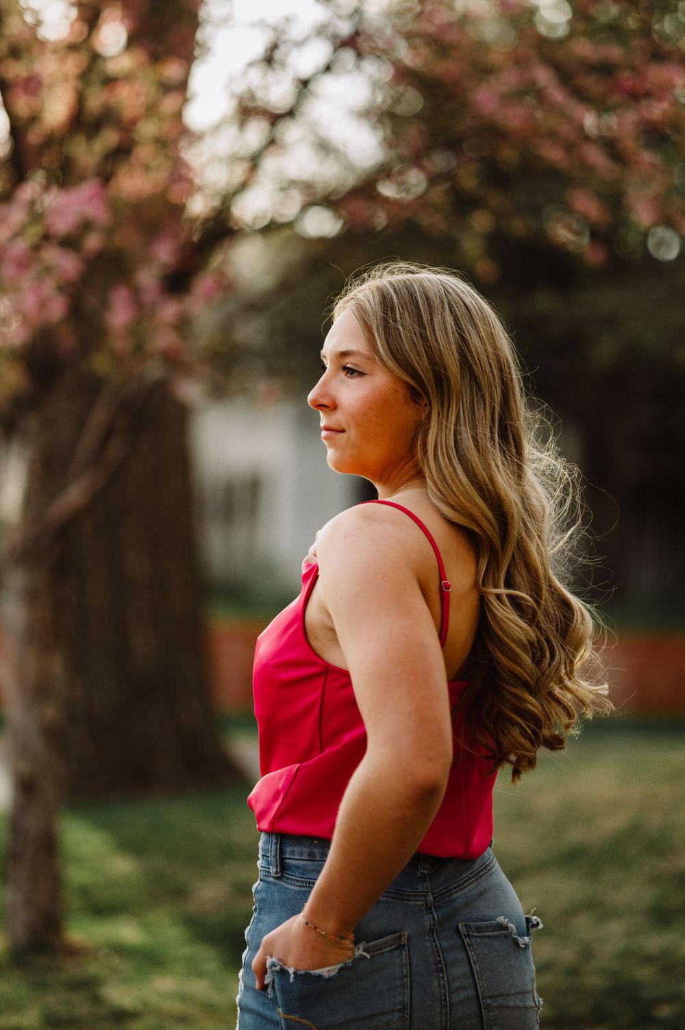 Woman in red tank top poses against blossoming trees during spring photoshoot.