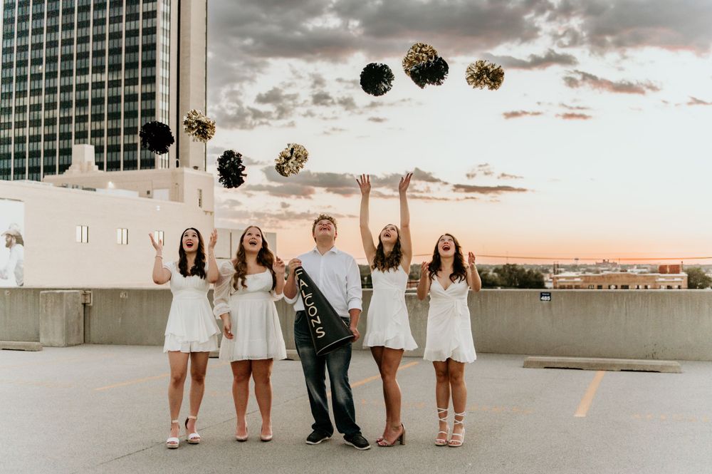 Group celebrates on rooftop during sunset with city skyline in background.