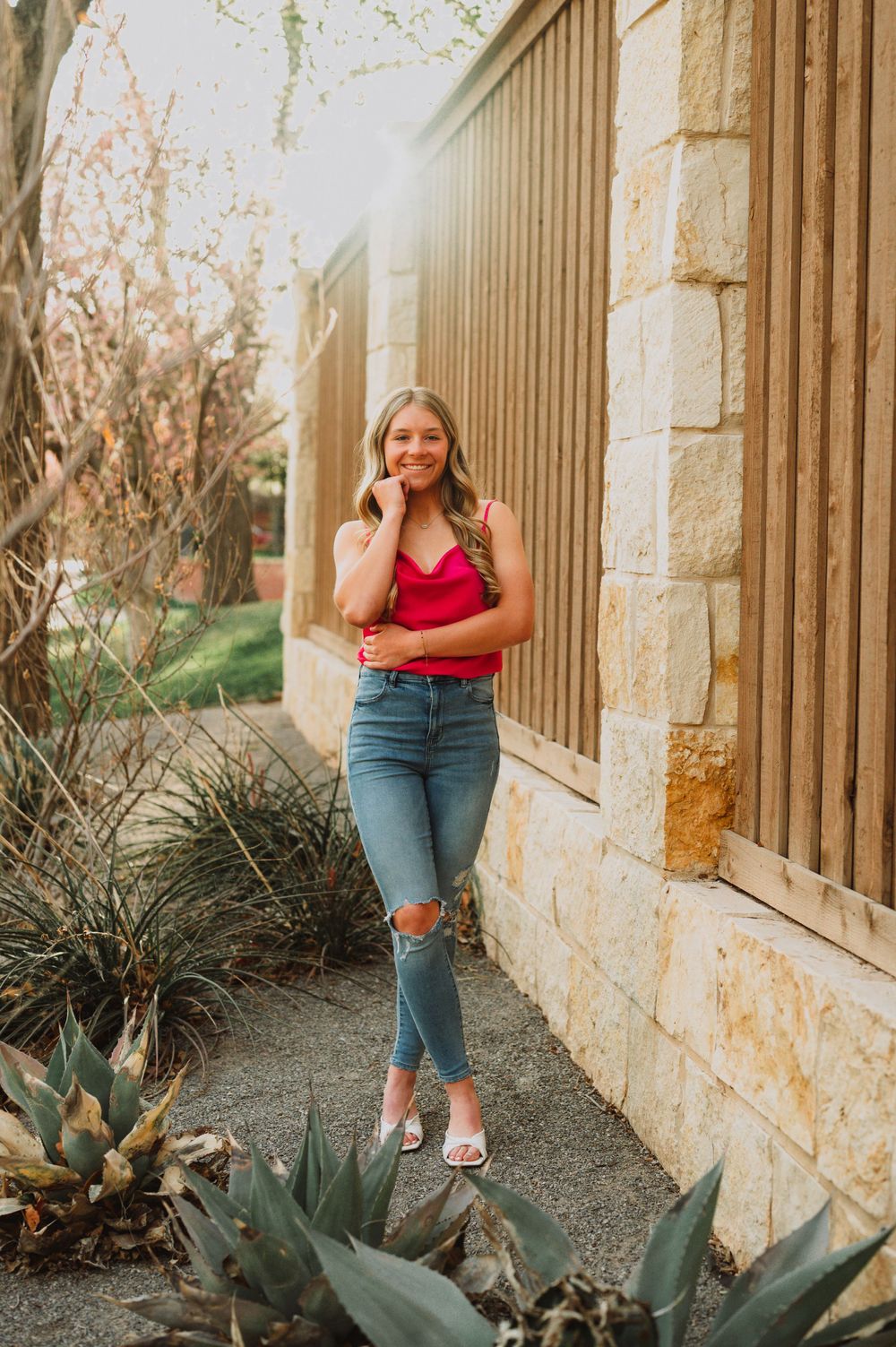 Woman in red top poses near stone building with desert landscaping.