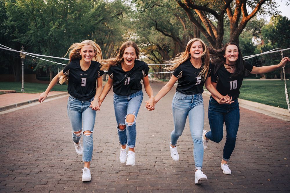 A playful group jumps in unison on a brick pathway during a casual outdoor photo session.