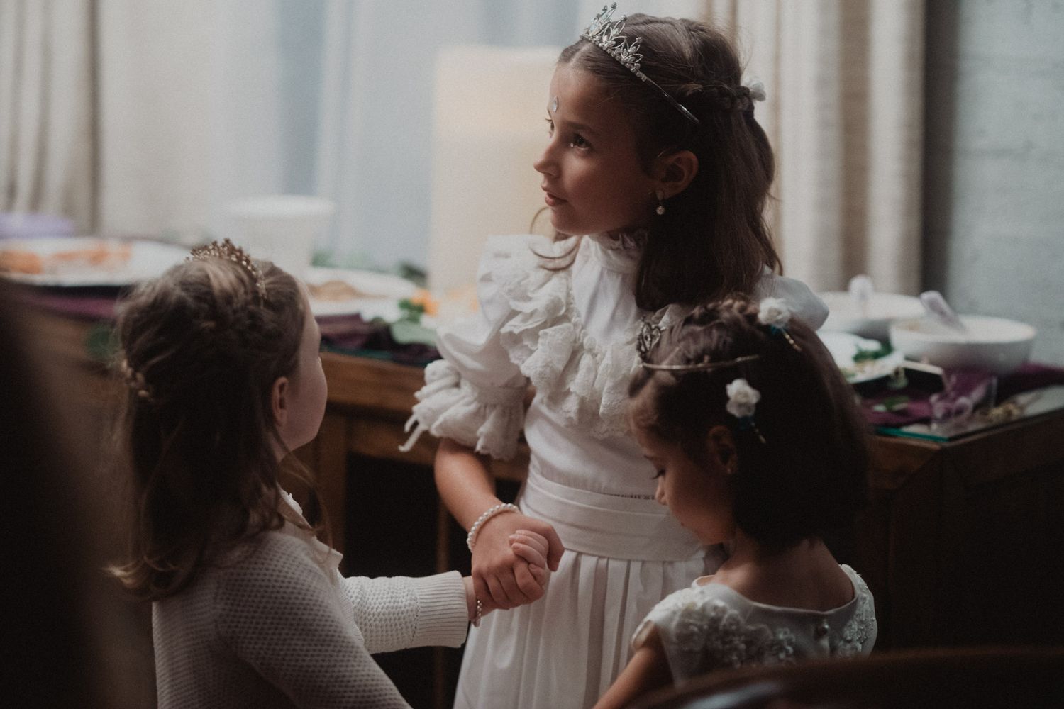 A bride in a white dress gets ready for her wedding day in a softly lit room.