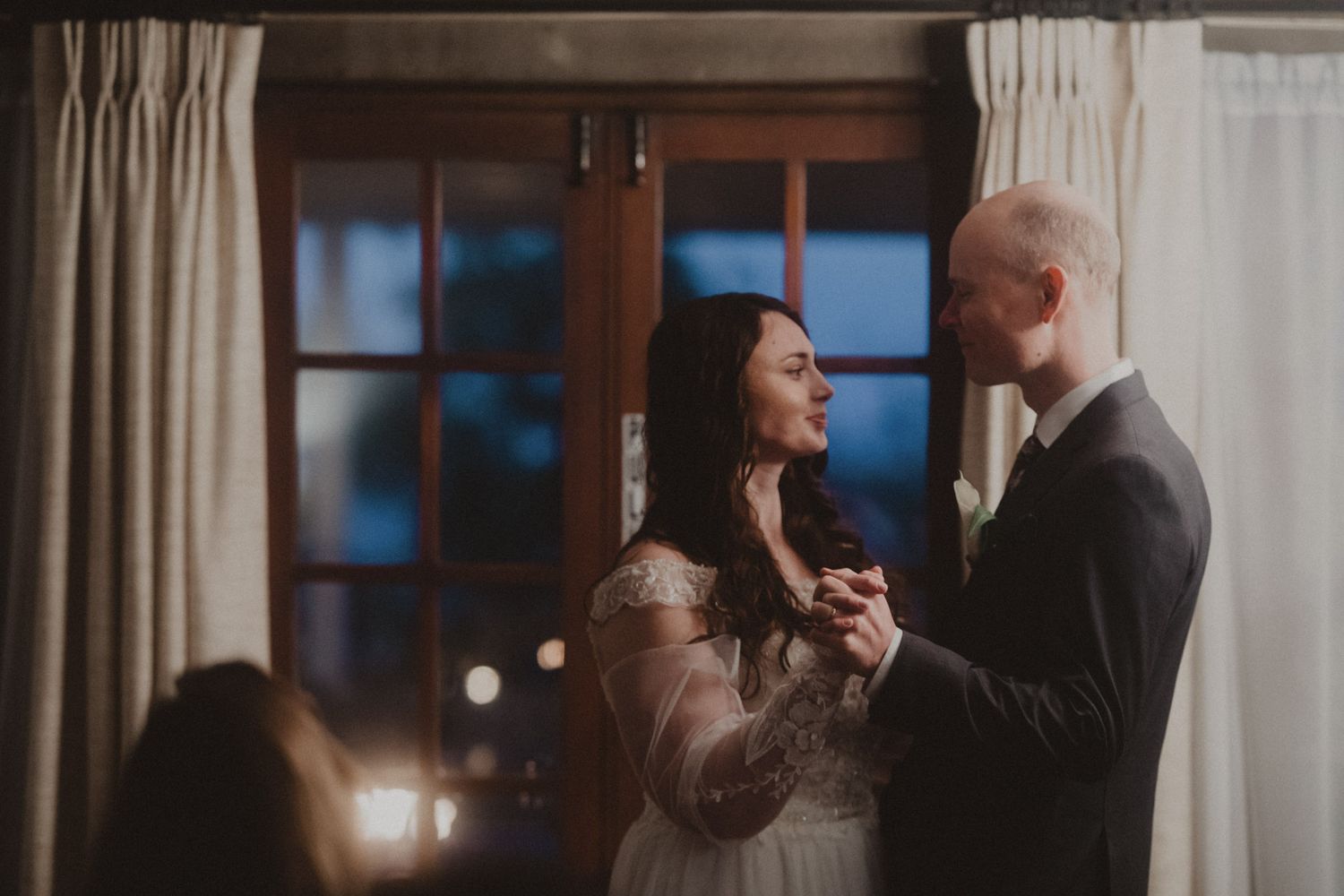 Wedding guests dance and celebrate together during an evening reception in a warmly lit indoor venue.