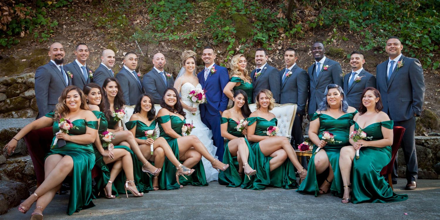 Wedding party in emerald green dresses poses together in outdoor garden setting.