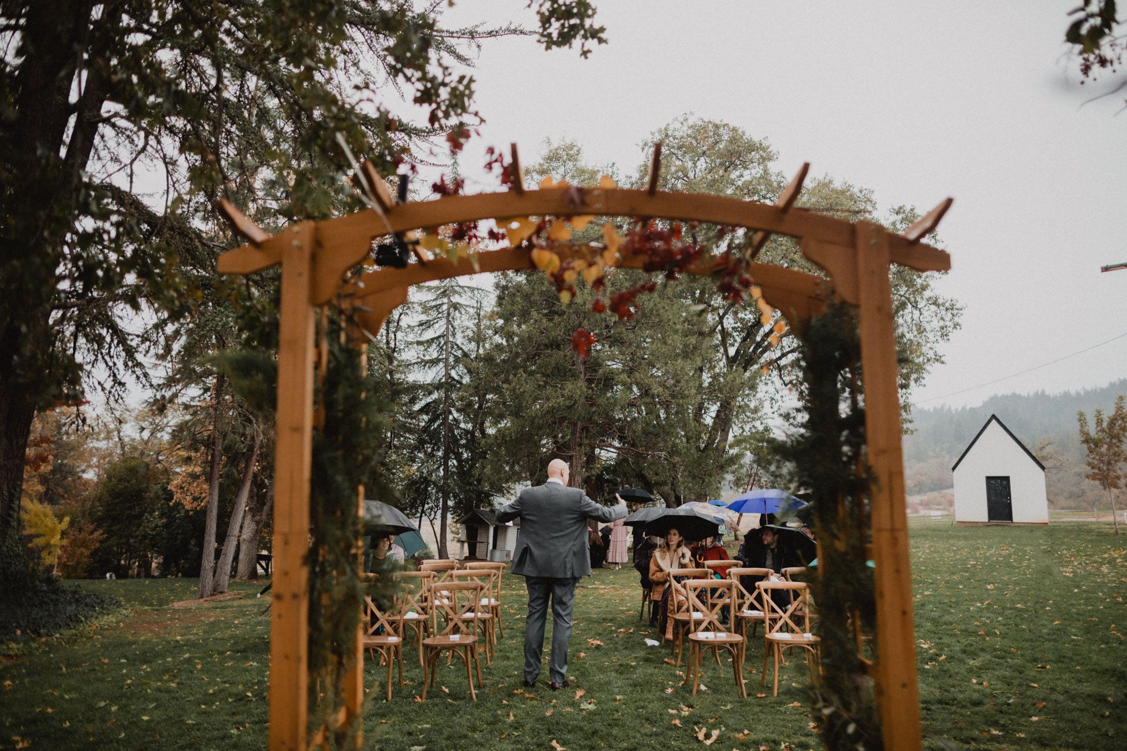 A rustic wooden wedding arch stands in an autumn garden setting with chairs arranged for an outdoor ceremony.