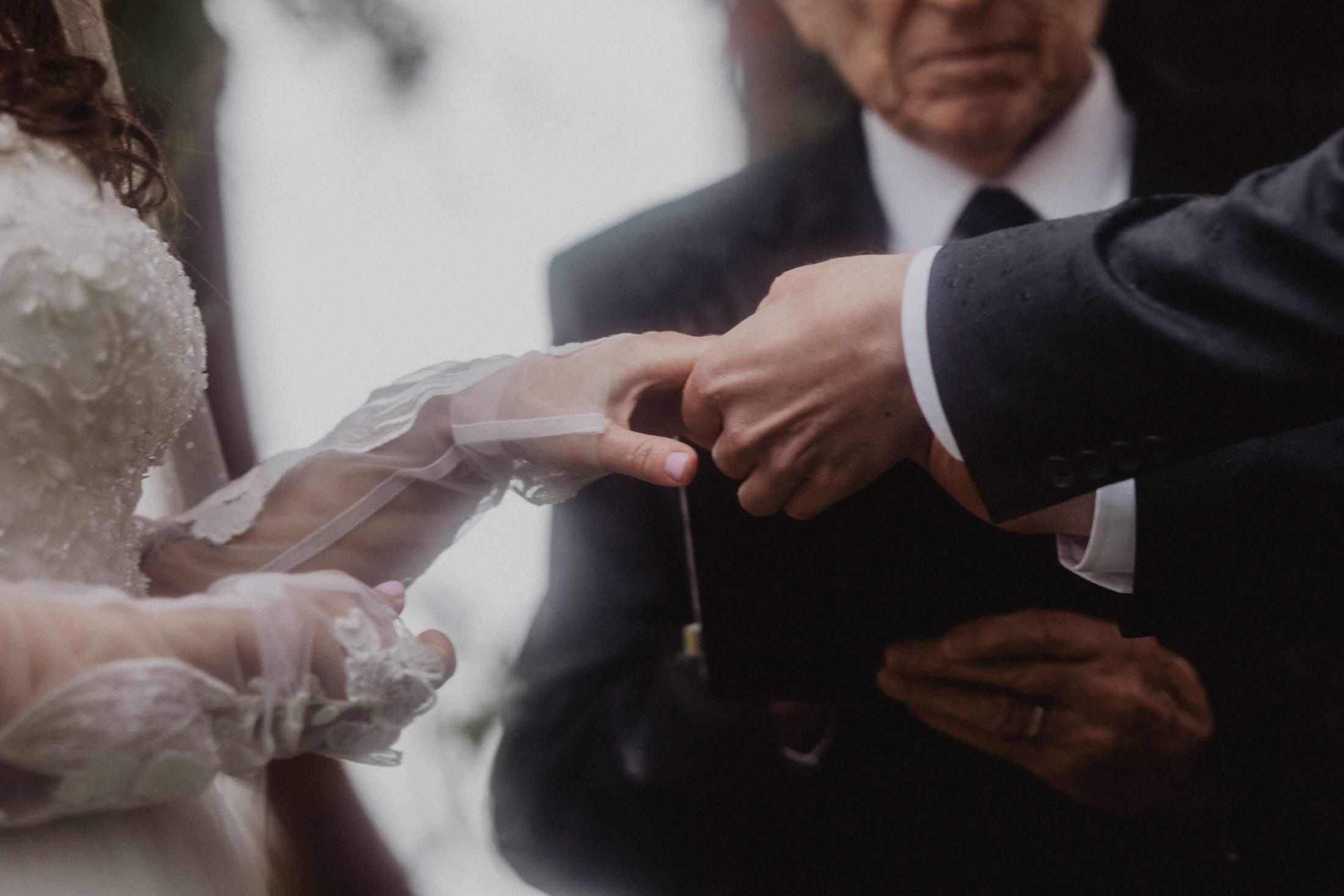 Intimate moment during a wedding ring exchange ceremony captured in dramatic lighting.