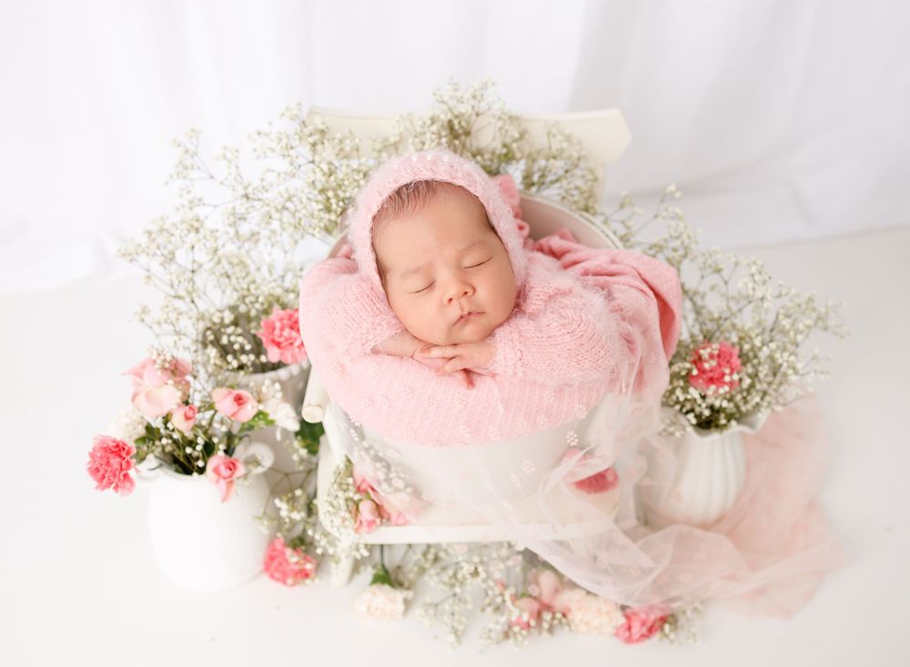 Newborn baby posed with pink flowers and soft white fabrics.