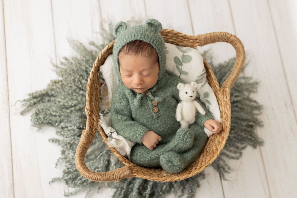 Sleeping newborn in sage green outfit nestled in woven basket.