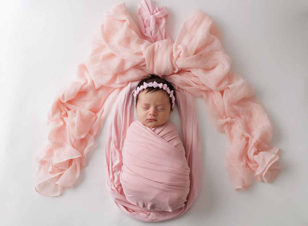 Artistic newborn portrait with flowing pink fabric arrangement.