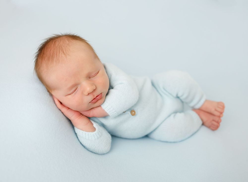 Sleeping infant wearing soft blue sleeper on light blue background.
