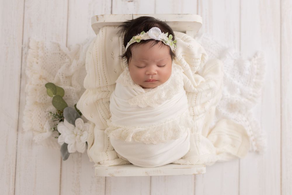 Sleeping baby wrapped in white fabric with delicate floral decorations.