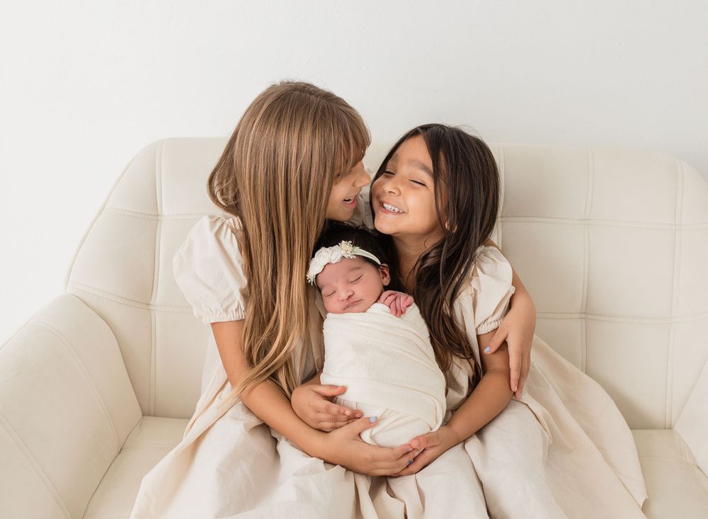 Siblings bonding during intimate indoor photo session on white furniture.