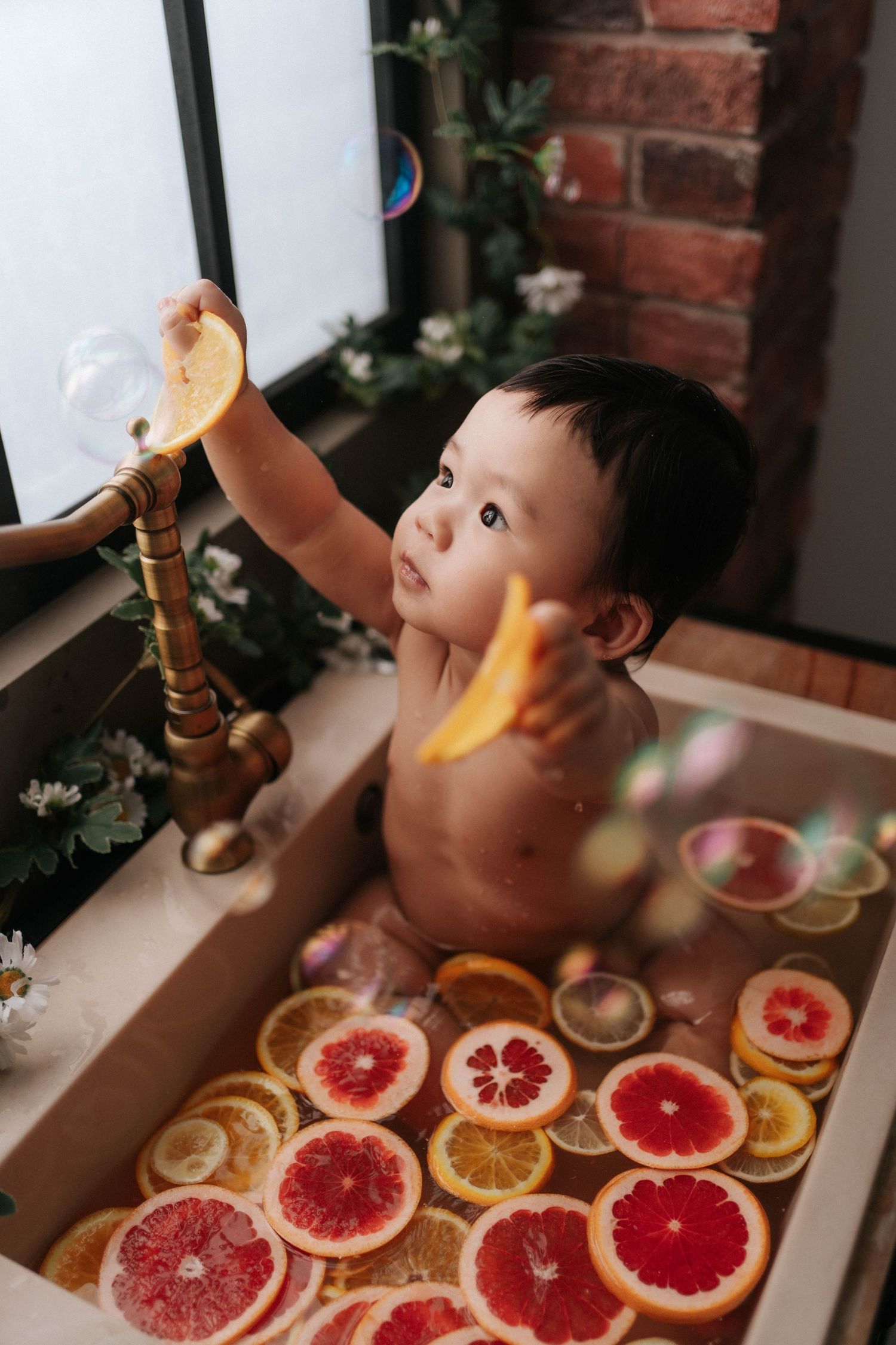 A child looks up curiously at citrus fruit slices arranged on a wooden table near exposed brick walls.