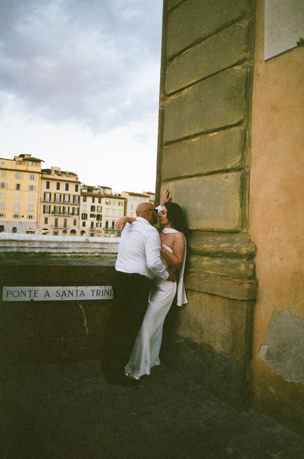 A series of candid shots showing a couple in white outfits leaning against a stone wall in an Italian city.