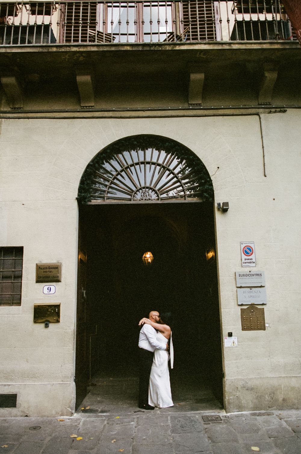 A sequence of arched doorways along a white stone building facade in an Italian street.