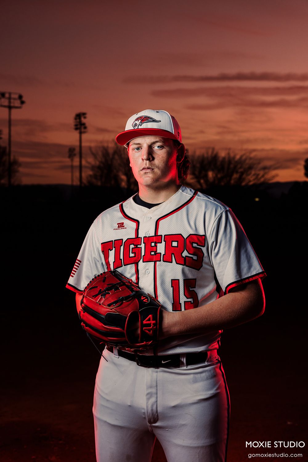 Baseball player displays red glove against orange sunset backdrop during team photo shoot.