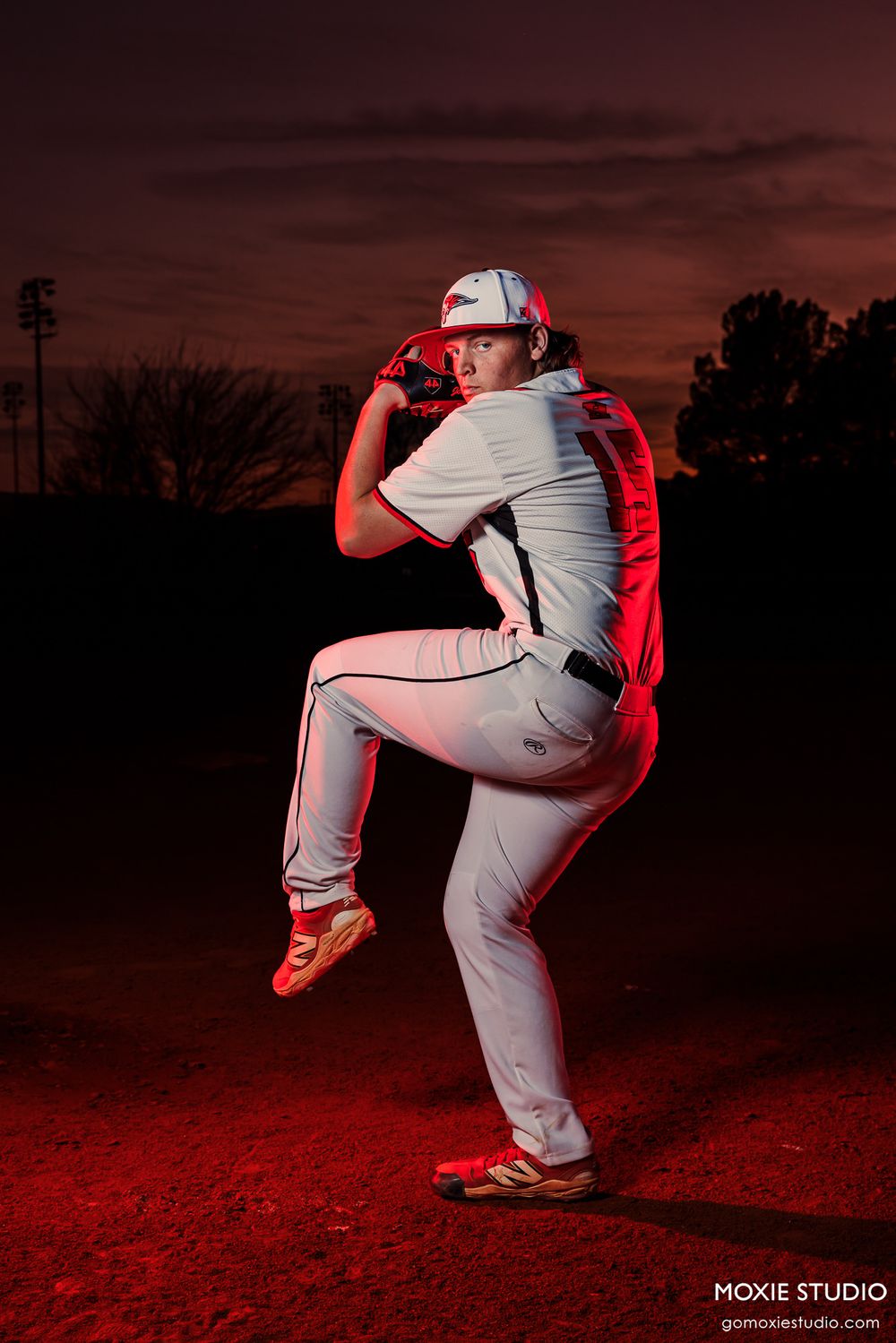 Baseball pitcher shown in dynamic sequence of wind-up motion against dramatic red sunset sky at dusk.