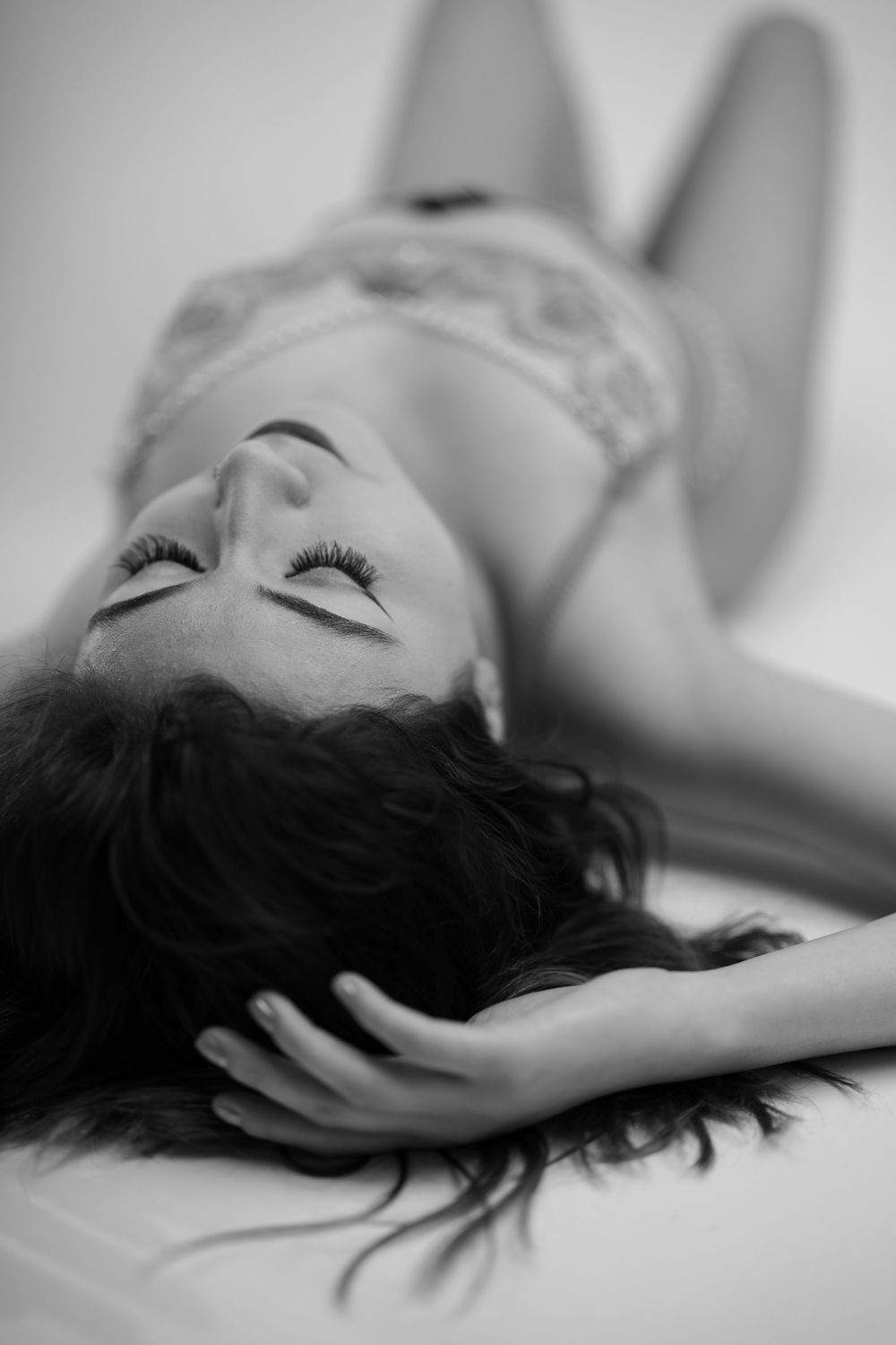 A black and white artistic portrait shows a person lying down with dark hair spread across a light surface.
