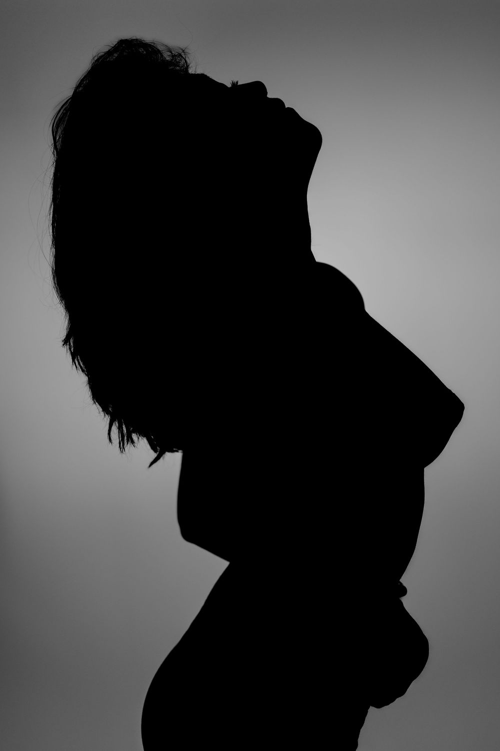 Dramatic silhouette profile against gray background shows figure leaning back with hair flowing.