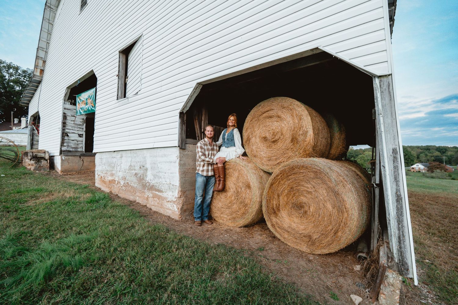 Large hay bales stacked against a white barn wall in a rural setting during daytime.
