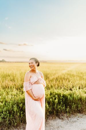 A person in a pink dress stands in a golden wheat field at sunset with warm glowing light.