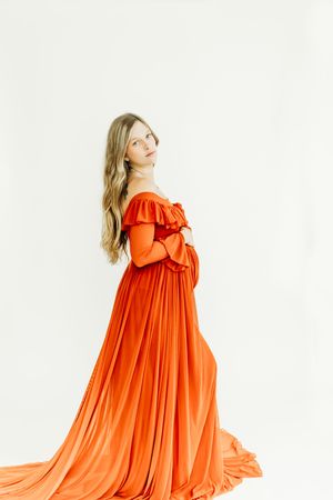 A flowing orange dress with dramatic ruffled neckline and billowing silhouette shown in four poses against white background.