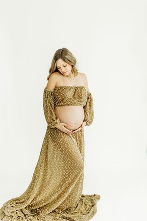 Maternity photo series showing an expectant mother in a flowing gold polka dot dress against a white backdrop.