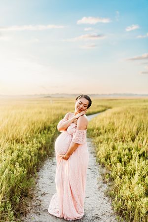 A dreamy scene shows someone dancing in a pink dress along a path between golden wheat fields at sunset.