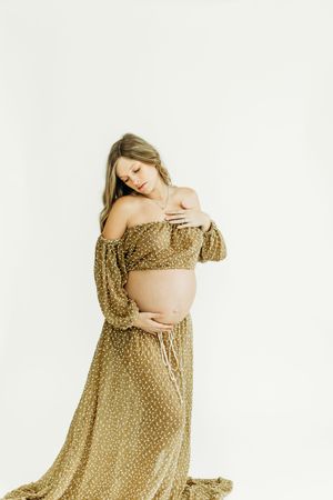 Elegant maternity portraits featuring a gold patterned dress in multiple graceful poses against white.