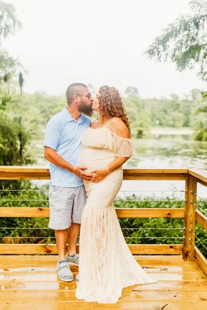 A couple shares a romantic moment on a wooden deck overlooking a scenic lake surrounded by greenery.