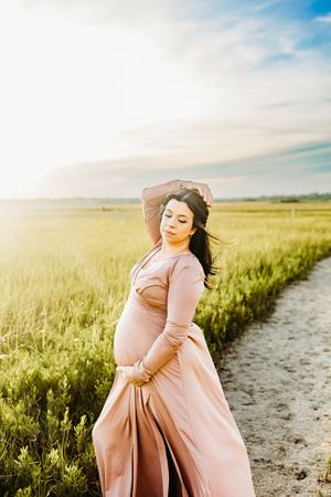 A person in a flowing pink dress twirls joyfully in a sunlit meadow beside a winding dirt path.