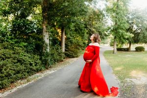 A figure in a flowing red dress walks along a tree-lined path creating a dramatic contrast against the green foliage.