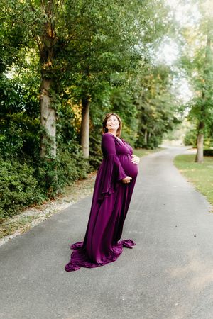 A person in a flowing purple dress poses dramatically on a tree-lined path during an autumn photoshoot.