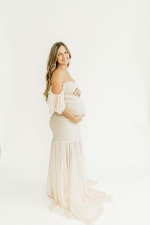 Dreamy maternity photography session with a flowing cream-colored dress in a bright studio setting.
